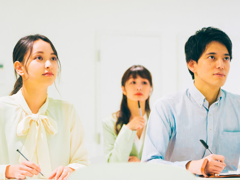 前に男性と女性、後ろに女性が座っていてメモを取りながらセミナーを熱心に聞いている写真